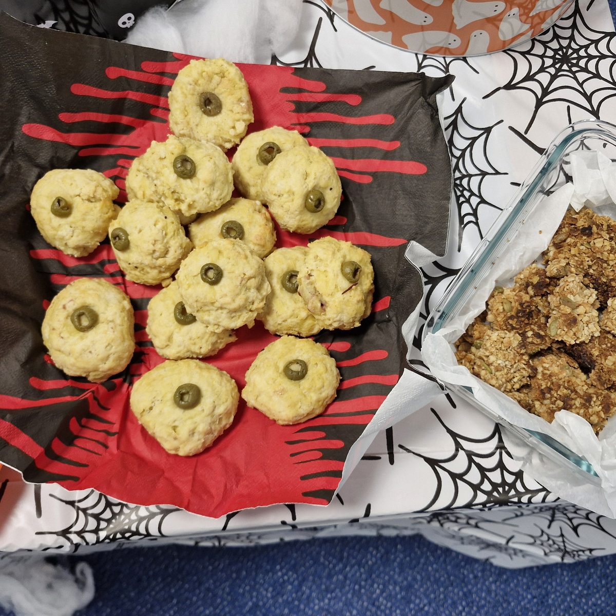 Eyeball cheese scones topped with green olives next to a dish of seeded flapjack