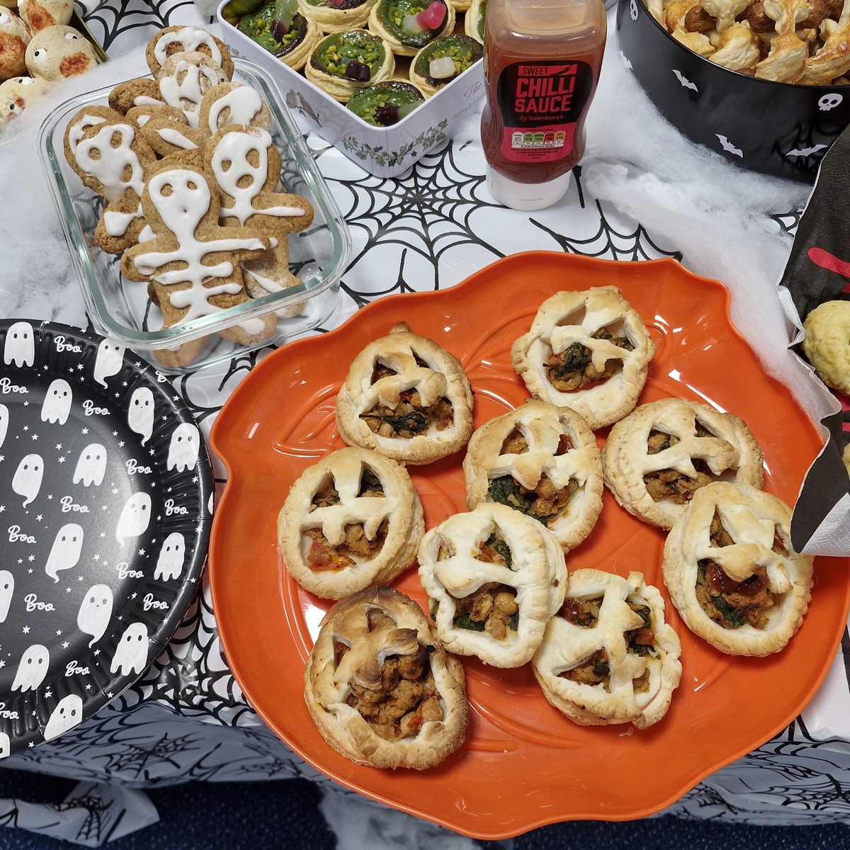 Jack o'lantern puff pastry tarts on an orange plate beside iced skeleton gingerbread men