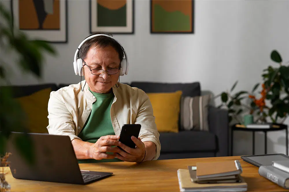 An older man using a smartphone, he is wearing headphones.