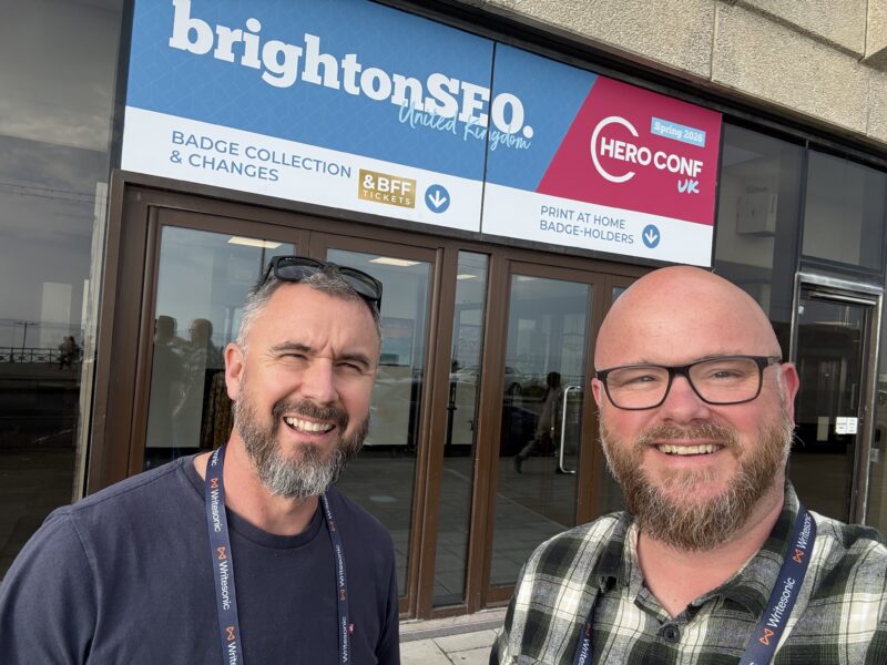 Paul and Nathan, co-founders of Priority Pixels, outside the brightonSEO and Hero Conf 2026 badge collection at the Brighton Centre.